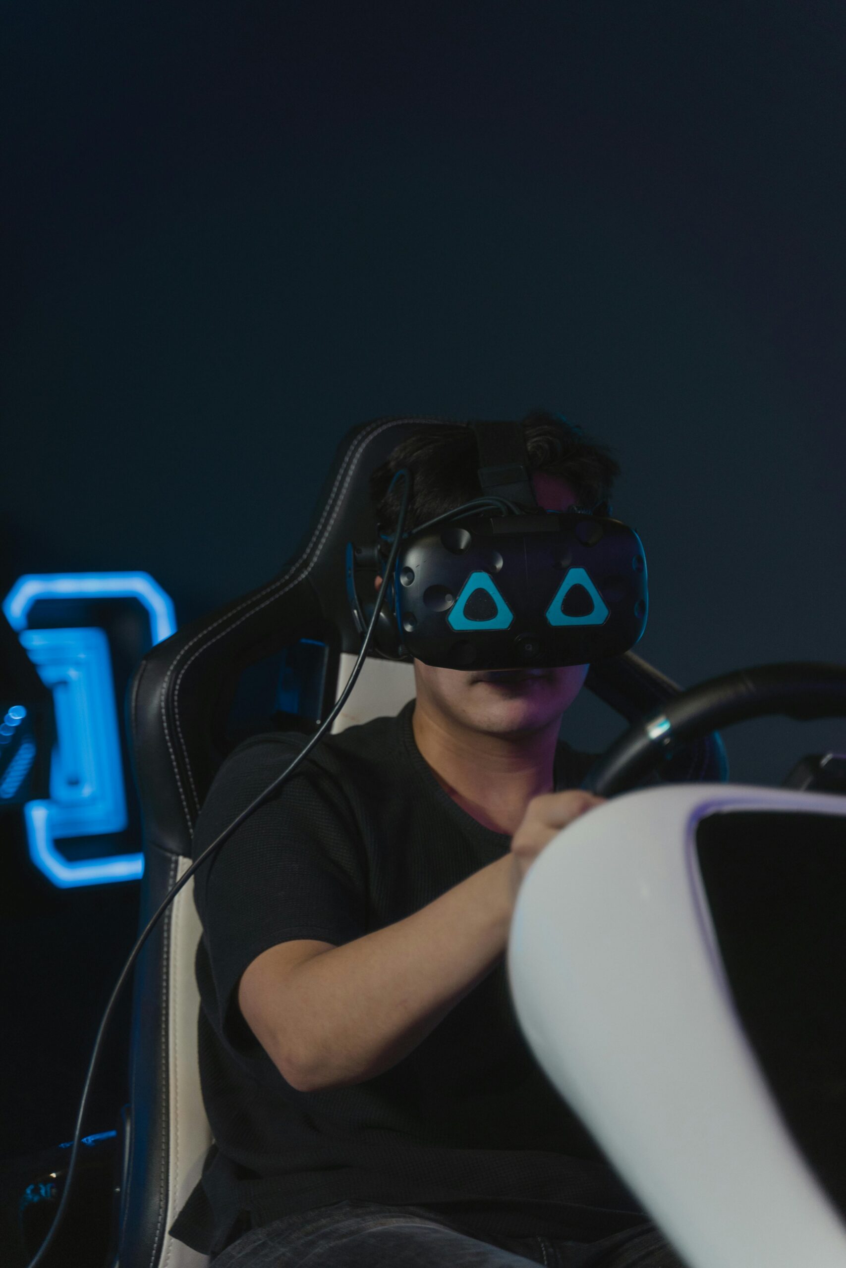 Adult male engaged in a virtual reality game, wearing VR headset and holding steering wheel.